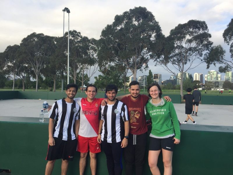 cuatro amigos futbolistas que miran a la cámara sonrientes. Dos de ellos con el uniforme de fútbol y están en el campo de césped de fútbol